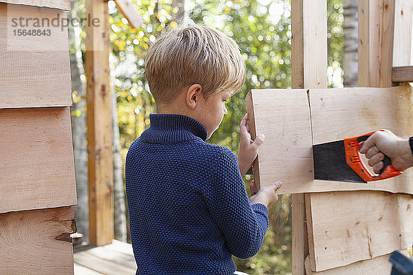 Junge lernt mit Erwachsenen Baumhaus bauen