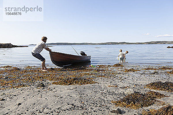 Vater zieht Boot an den Strand  Söhne spielen in der Nähe  Norwegen