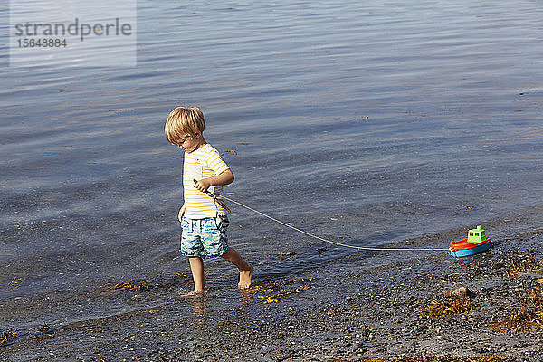 Junge spielt mit Spielzeugboot am Strand