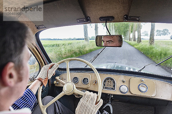 Mann fährt Oldtimer auf Landstraße