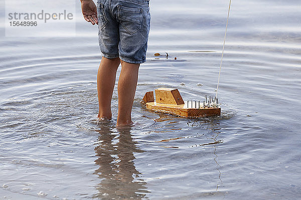 Junge spielt mit Holzspielzeugboot im Wasser