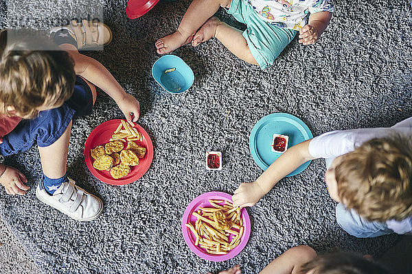Kinder genießen Teller mit Essen auf dem Teppich