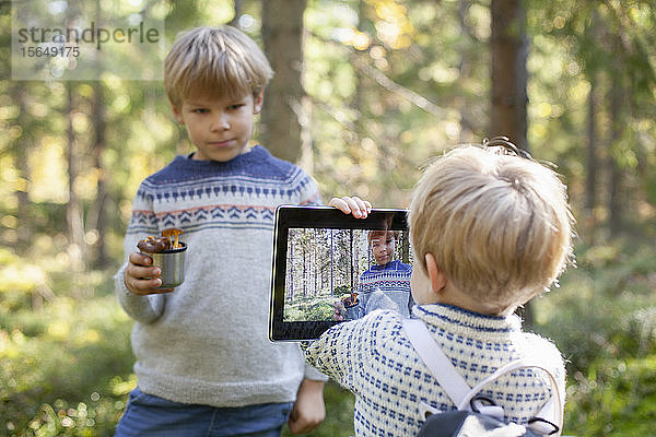 Kleinkind fotografiert Bruder mit Tasse Waldpilze im Wald