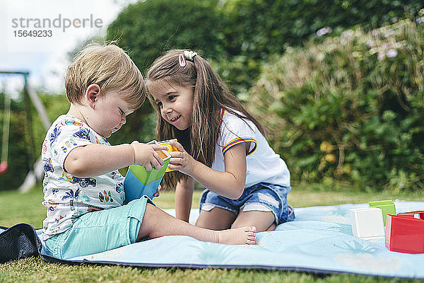 Schwestern spielen mit Blöcken auf einer Picknickdecke