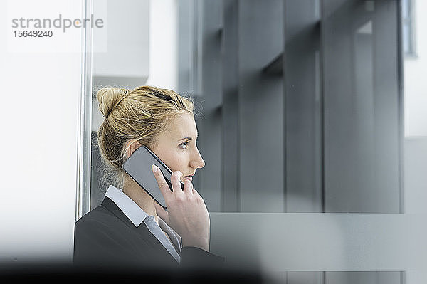 Junge Geschäftsfrau spricht mit einem Smartphone im Flur des Bürogebäudes