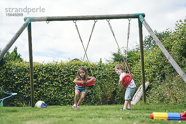 Mädchen und Junge drehen sich auf Schaukeln im Garten