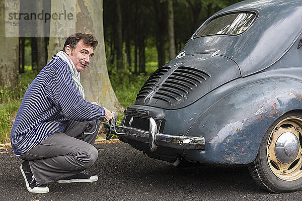 Mann repariert Oldtimer auf Landstraße