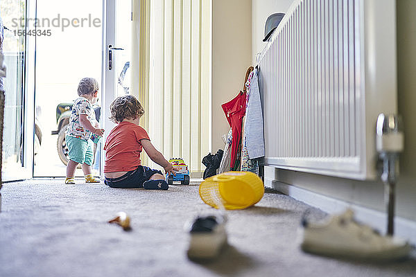 Jungen spielen mit Spielzeuglastwagen und verschiedenen Spielsachen auf dem Teppich