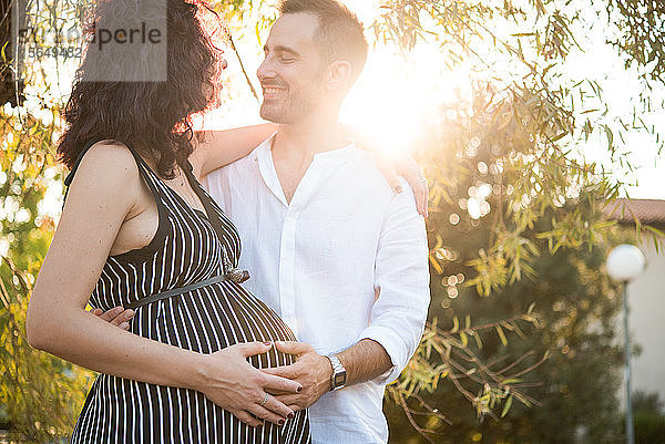 Mann lächelt und berührt den Bauch einer schwangeren Frau im Park