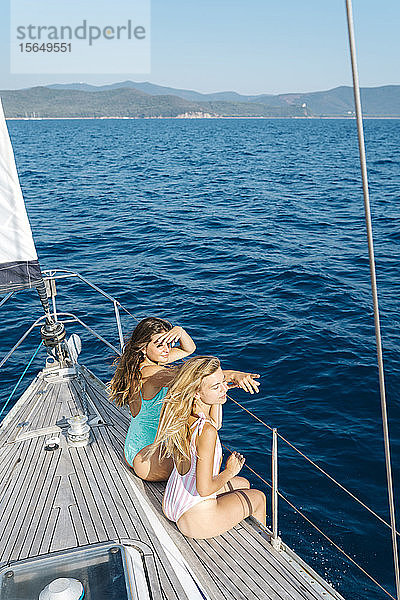 Freunde entspannen sich auf der Deckskante eines Segelbootes  Italien
