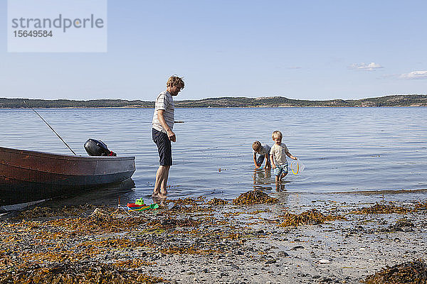 Vater und Söhne spielen neben dem am Strand vertäuten Boot  Norwegen
