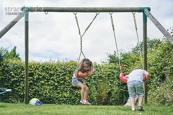 Mädchen und Junge drehen sich auf Schaukeln im Garten