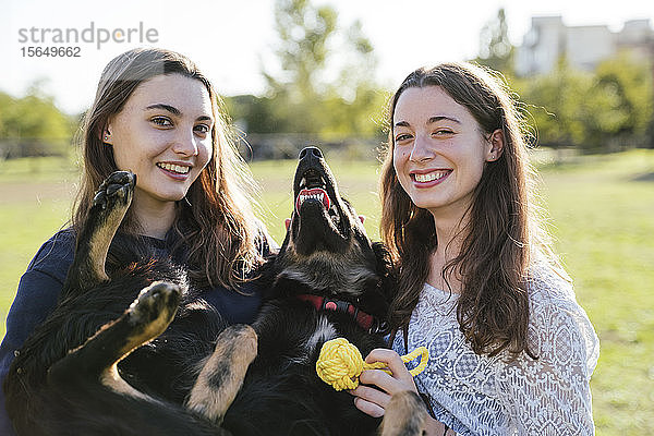 Schwestern spielen mit Hund im Park