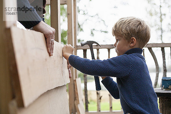 Junge lernt mit Erwachsenen Baumhaus bauen
