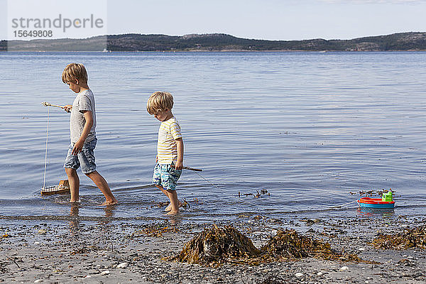 Brüder spielen mit Spielzeugboot am Strand