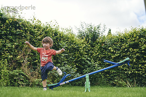 Junge hüpft von Spielzeugwippe im Garten