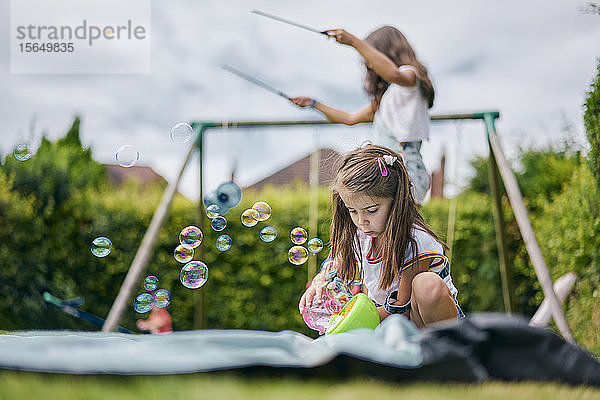 Mädchen spielt mit Seifenblasen  Schwester im Hintergrund mit Diabolo