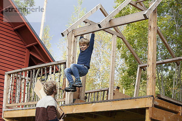 Vater beobachtet Jungen  der auf dem Balken eines unvollendeten Baumhauses schwingt