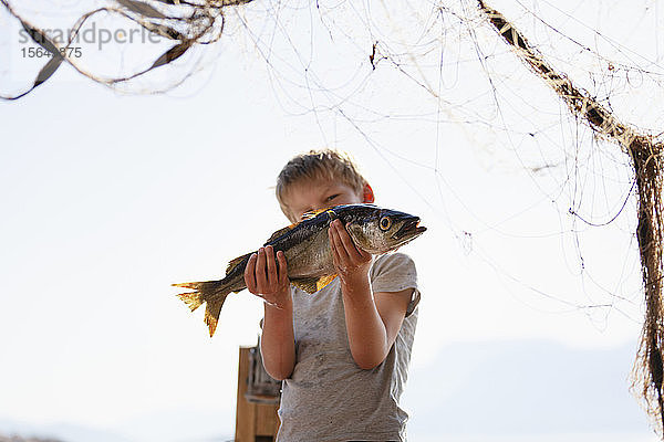 Junge hält Fisch hoch  Fischernetz im Vordergrund