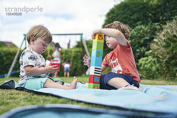 Bruder und kleine Schwester spielen mit Blöcken auf einer Picknickdecke