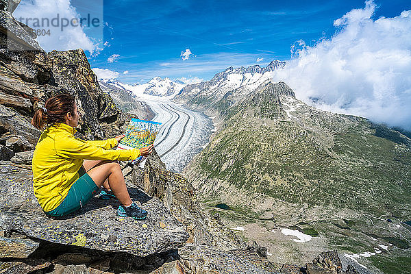 Frau  die auf einem Felsen sitzend eine Karte betrachtet  am Aussichtspunkt Eggishorn oberhalb des Aletschgletschers  Berner Alpen  Kanton Wallis  Schweiz