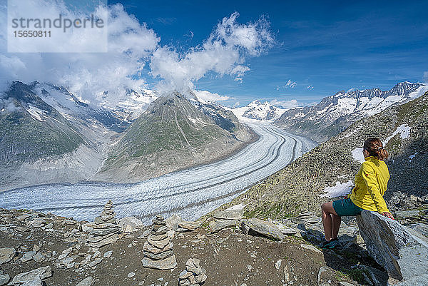 Seitenansicht einer Frau  die auf einem Felsen sitzt und den Aletschgletscher vom Aussichtspunkt Eggishorn aus bewundert  Berner Alpen  Kanton Wallis  Schweiz