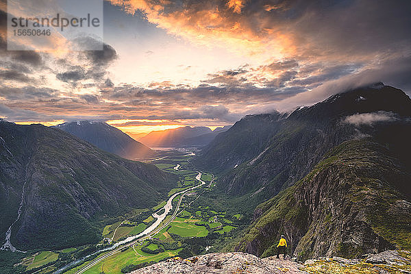 Erhöhte Ansicht eines Mannes  der auf dem Bergrücken Romsdalseggen steht und das Rauma-Tal bei Sonnenuntergang bewundert  Andalsnes  More og Romsdal  Norwegen  Skandinavien