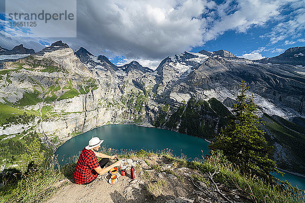 Wanderer kocht Essen auf einem Campingkocher hoch über dem Oeschinensee  Berner Oberland  Kandersteg  Kanton Bern  Schweiz