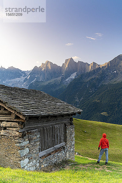 Rückansicht eines Mannes aus einer Steinhütte mit Blick auf den Piz Cengalo und Badile  Tombal  Bergell  Kanton Graubünden  Schweiz