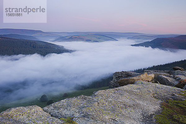 Die Morgendämmerung bricht über den Hügeln des Peak District mit einer Wolkeninversion über dem Ladybower Reservoir unterhalb von Bamford Edge  Peak District  Derbyshire  England  Vereinigtes Königreich