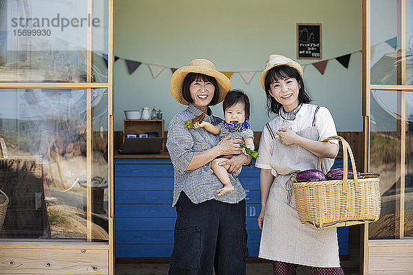 Zwei Japanerinnen und ein Junge stehen vor einem Bauernladen und lächeln in die Kamera.