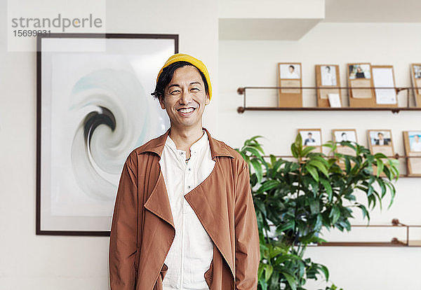 Männlicher japanischer Profi  der in einem Arbeitsraum steht und in die Kamera lächelt.