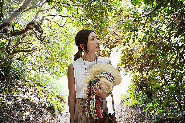 Japanische Frau mit Hut  die in einem Wald wandert.