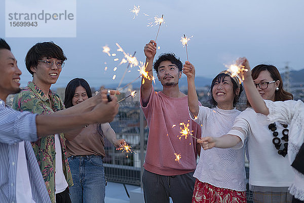 Gruppe junger japanischer Männer und Frauen mit Wunderkerzen auf einem Dach in einer städtischen Umgebung.