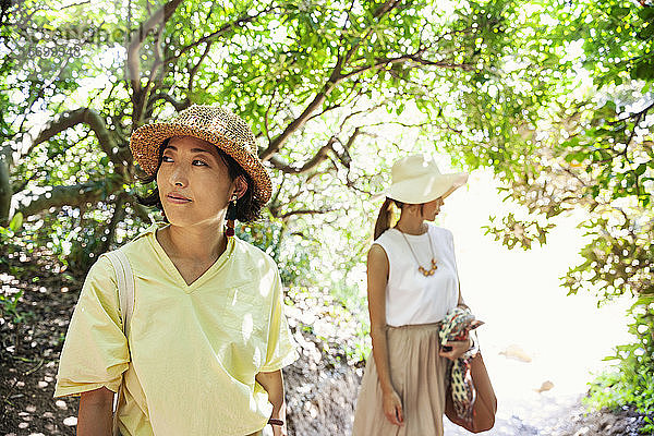 Zwei Japanerinnen mit Hüten  die in einem Wald wandern.