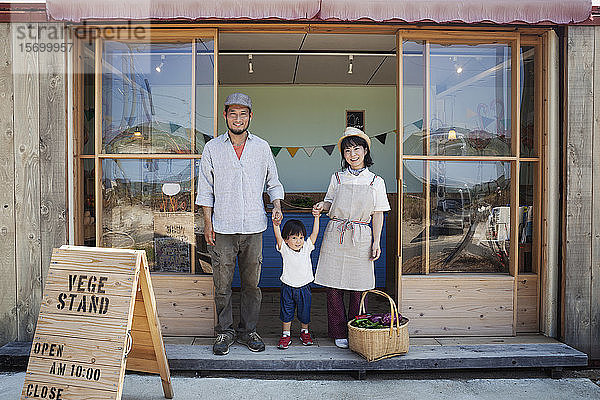 Japanischer Mann  Frau und Junge stehen vor einem Bauernladen  halten sich an den Händen und schauen in die Kamera.
