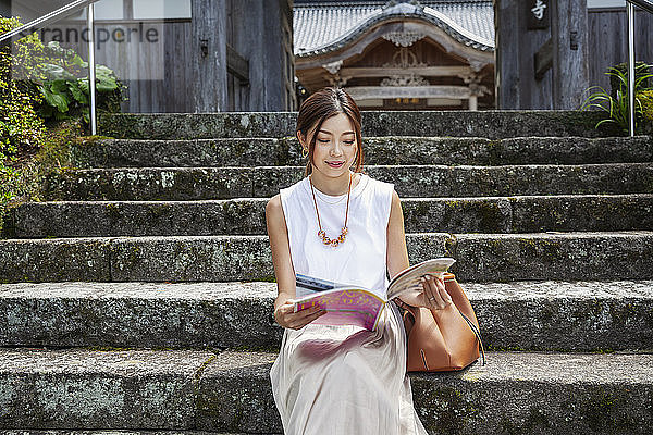 Japanerin  die auf Stufen vor einem buddhistischen Tempel sitzt.
