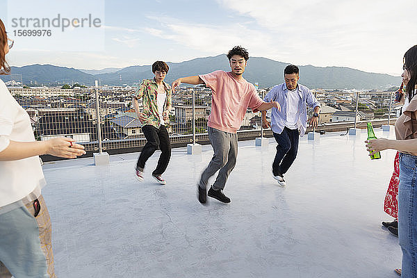 Gruppe junger japanischer Männer und Frauen  die auf einem Dach in einer städtischen Umgebung tanzen.