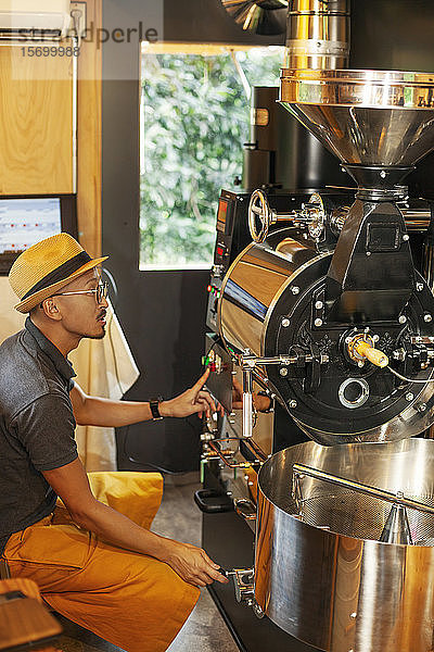 Japanischer Mann mit Hut und Brille sitzt in einem Öko-Café und bedient eine Kaffeeröstmaschine.