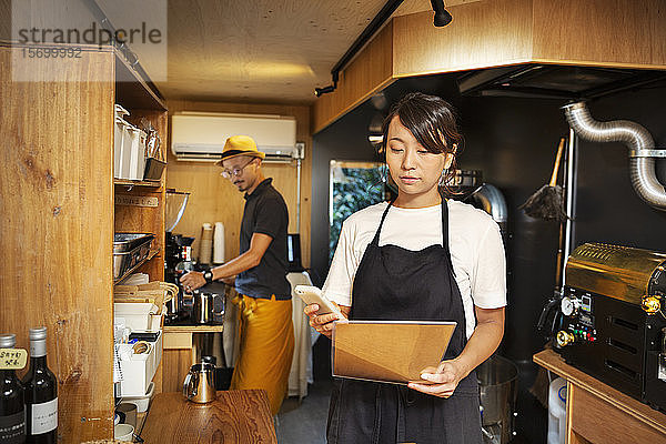 Japanerin und Japaner arbeiten in einem Öko-Café  bereiten Kaffee zu und benutzen ein Mobiltelefon.
