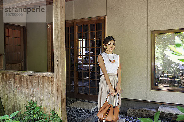 Japanische Frau steht auf einer Veranda und hält eine Handtasche.