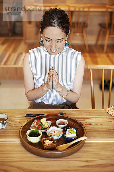 Schrägaufnahme einer Japanerin  die in einem Café vor einer Auswahl vegetarischer Speisen sitzt.