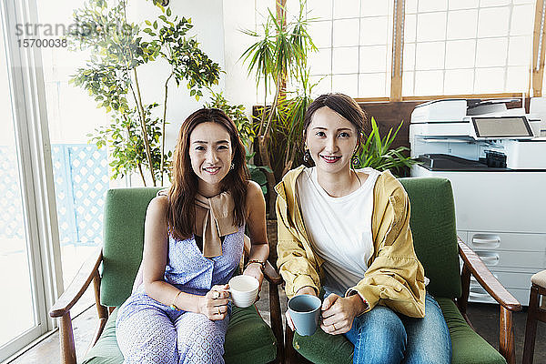 Zwei japanische Fachfrauen sitzen in einem Arbeitsraum und lächeln in die Kamera.
