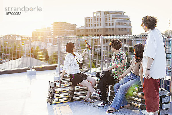 Gruppe junger japanischer Männer und Frauen  die auf einem Dach in einer städtischen Umgebung sitzen.