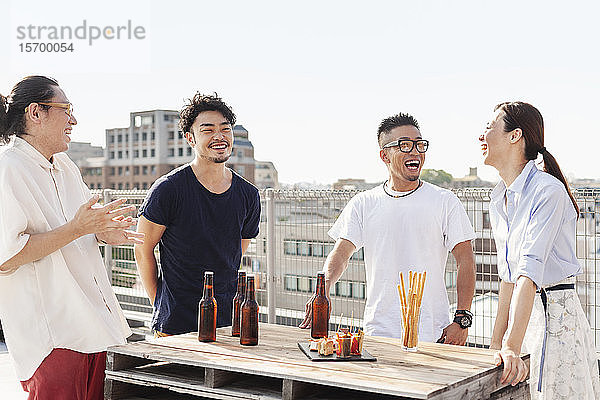 Gruppe junger japanischer Männer und Frauen  die auf einem Dach in einer städtischen Umgebung stehen und Bier trinken.