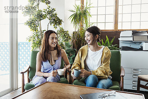 Zwei japanische Fachfrauen sitzen in einem Arbeitsraum und lächeln sich an.