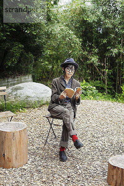 Japanerin mit Brille und Hut sitzt auf einem Stuhl vor dem Eco Cafe und liest ein Buch.