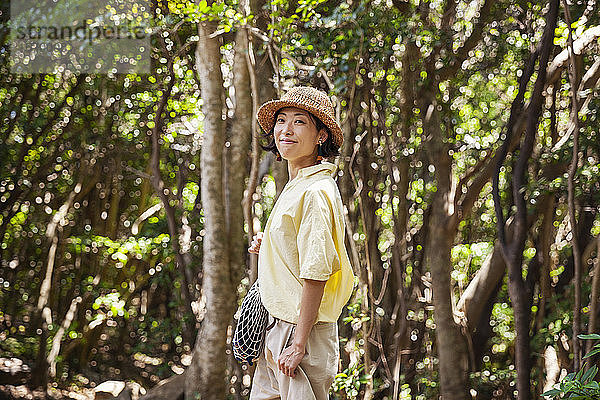 Japanische Frau mit Hut beim Wandern im Wald.