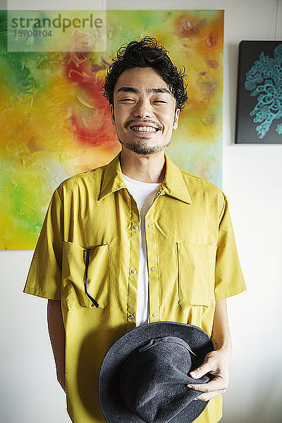 Japanischer Mann steht vor einem abstrakten Gemälde in einer Kunstgalerie und lächelt in die Kamera.