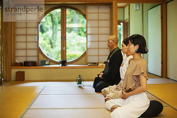 Zwei Japanerinnen und ein buddhistischer Priester knien im buddhistischen Tempel und beten.